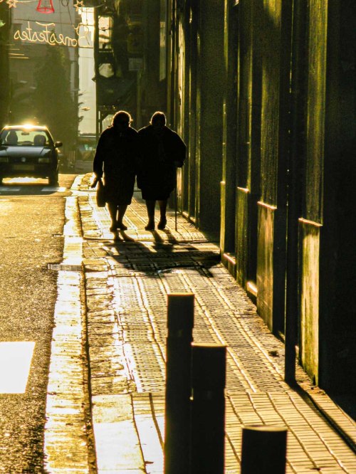 Two women walk on a street in Barcelona at sunset