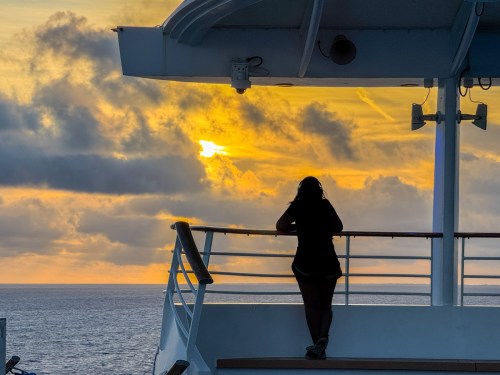 Woman in silhouette watches sunrise from Independence of the Seas aft