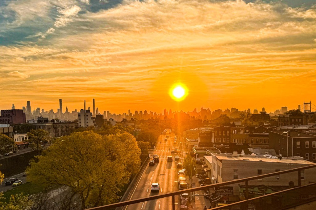 A stunning sunset view over New York City, with the skyline silhouetted against a vibrant orange sky and the setting sun casting warm light on the landscape.